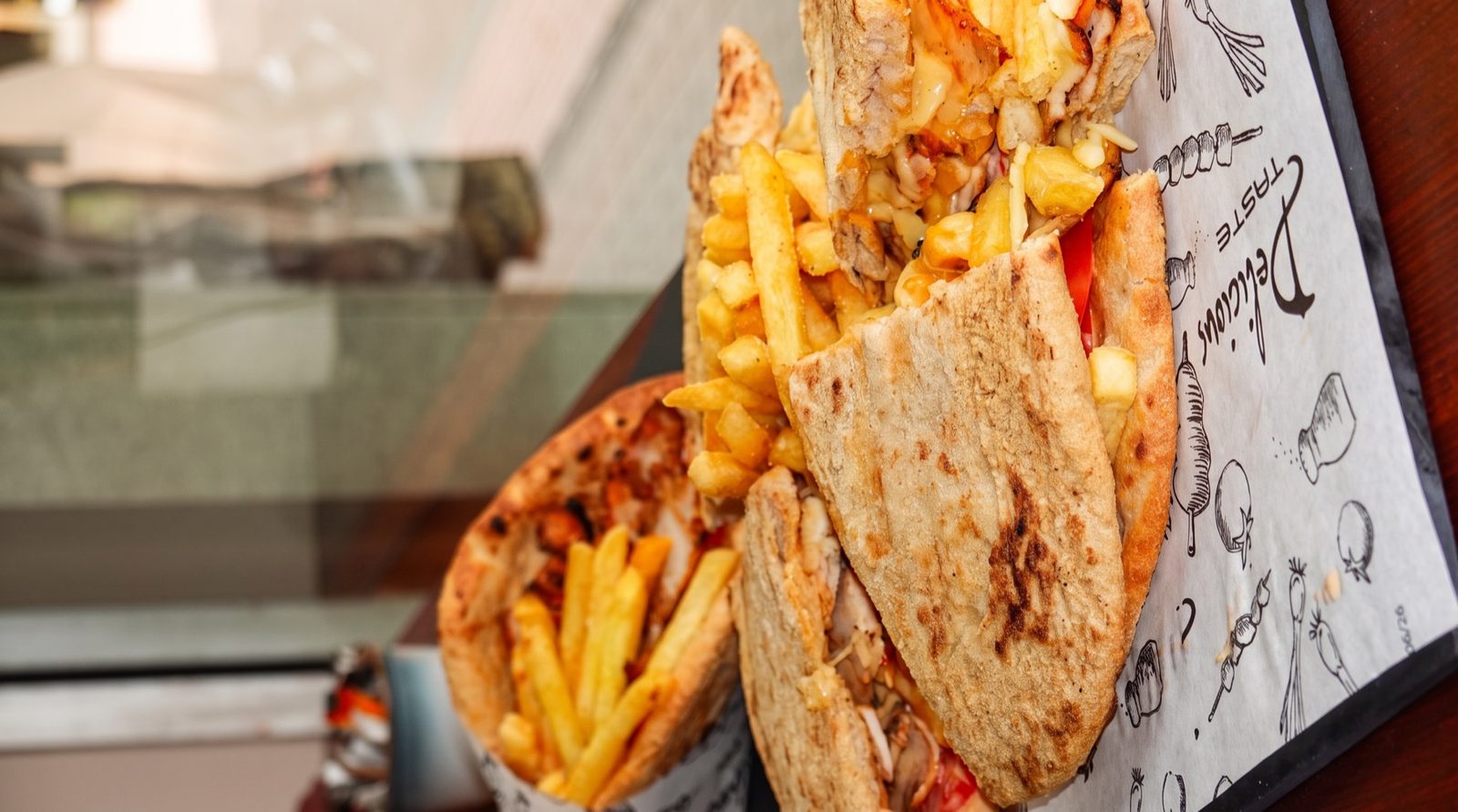 Two loaded pita gyros with chips on branded Greek Spot paper